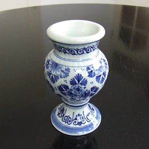 May include: A small, white ceramic vase with a blue and white floral pattern. The vase has a round body and a flared top.