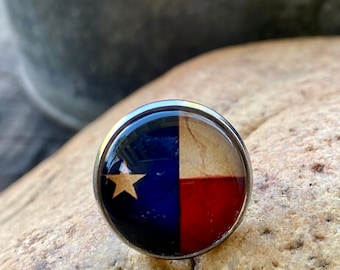May include: A silver ring with a round, blue, white, and red Texas flag design.