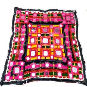 Può includere: Un cuscino quadrato con un design a patchwork colorato che presenta piccoli specchi, ricami e motivi geometrici in tonalità di rosa, rosso, verde, giallo e nero.