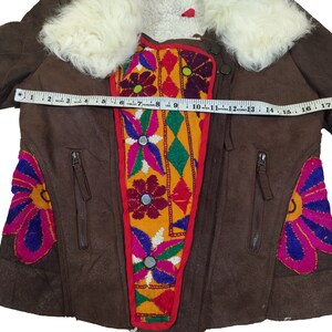 K&ouml;nnte beinhalten: Braune Wildlederjacke mit cremefarbenem Pelzkragen. Die Jacke hat bunte Blumenstickereien und Rei&szlig;verschlusstaschen. Die Jacke misst ca. 46 cm &uuml;ber der Brust.