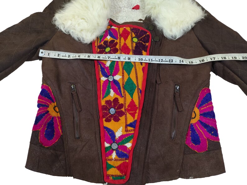 K&ouml;nnte beinhalten: Braune Wildlederjacke mit cremefarbenem Pelzkragen. Die Jacke hat bunte Blumenstickereien und Rei&szlig;verschlusstaschen. Die Jacke misst ca. 46 cm &uuml;ber der Brust.