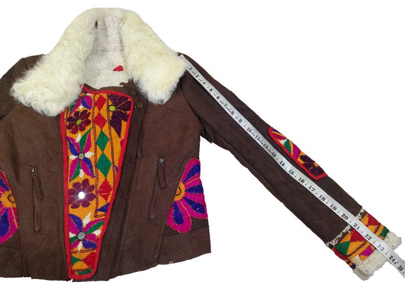 K&ouml;nnte beinhalten: Braune Wildlederjacke mit cremefarbenem Shearling-Kragen und -Futter. Die Jacke hat bunte, gestickte Blumen- und geometrische Designs auf der Vorderseite und den &Auml;rmeln. Die &Auml;rmell&auml;nge betr&auml;gt ca. 61 cm.