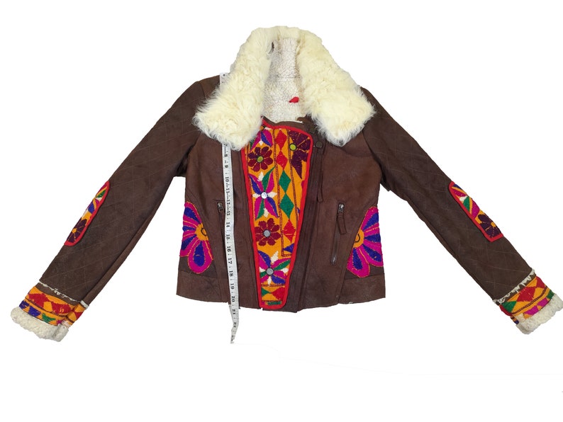 K&ouml;nnte beinhalten: Braune Wildlederjacke mit cremefarbenem Kunstfellkragen. Die Jacke hat bunte, gestickte Blumen- und geometrische Muster auf der Vorderseite, den &Auml;rmeln und den Manschetten. Ein Ma&szlig;band ist auf der Jacke platziert. Die Jacke hat einen Rei&szlig;verschluss.