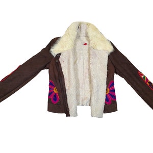 K&ouml;nnte beinhalten: Braune Jacke mit cremefarbenem Shearling-Futter und -Kragen. Die Jacke hat bunte Blumen- und geometrische Stickereidetails an den &Auml;rmeln und der Vorderseite. Die Jacke hat einen Knopfverschluss und ein Steppmuster.