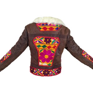 K&ouml;nnte beinhalten: Braune Jacke mit farbenfrohen Blumenstickereien auf dem R&uuml;cken und den &Auml;rmeln. Die Jacke hat einen wei&szlig;en Fellkragen und -b&uuml;ndchen. Die Stickerei weist rote, gelbe, rosa und blaue Akzente auf. Die Jacke besteht aus einem strukturierten Material.