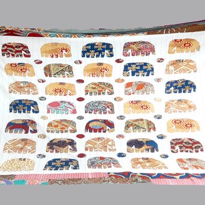 K&ouml;nnte beinhalten: Wei&szlig;e Baumwolldecke mit Patchwork-Bord&uuml;re. Die Decke zeigt ein sich wiederholendes Muster aus wei&szlig;en Elefanten mit farbenfrohen gemusterten K&ouml;rpern. Die Elefanten sind in Reihen angeordnet und von kleinen, bunten Kreisen umgeben.