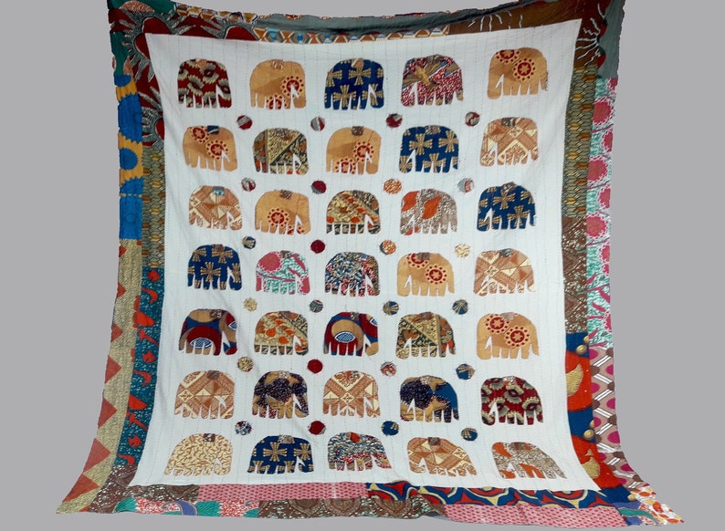 K&ouml;nnte beinhalten: Wei&szlig;e Baumwoll-Decke mit Patchwork-Muster, das bunte Elefantenmotive zeigt. Die Elefanten sind aus verschiedenen Stoffen gefertigt und haben unterschiedliche Muster.