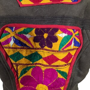 K&ouml;nnte beinhalten: Nahaufnahme einer braunen Lederjacke mit bunten gestickten Aufn&auml;hern. Die Aufn&auml;her zeigen florale und geometrische Designs in Gelb-, Rosa-, Gr&uuml;n-, Blau- und Lilat&ouml;nen, umrandet in Rot.