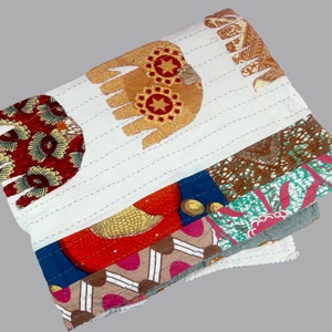 K&ouml;nnte beinhalten: Eine wei&szlig;e Baumwolldecke mit Patchwork-Muster aus verschiedenen bunten Stoffen. Die Decke hat ein handgen&auml;htes Muster und enth&auml;lt ein Design eines Elefanten mit Sternen und Kreisen.