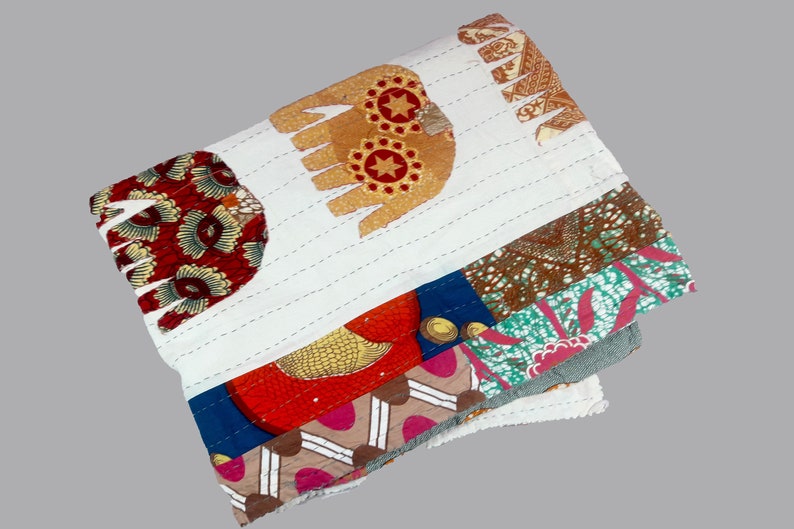 K&ouml;nnte beinhalten: Eine wei&szlig;e Baumwolldecke mit Patchwork-Muster aus verschiedenen bunten Stoffen. Die Decke hat ein handgen&auml;htes Muster und enth&auml;lt ein Design eines Elefanten mit Sternen und Kreisen.