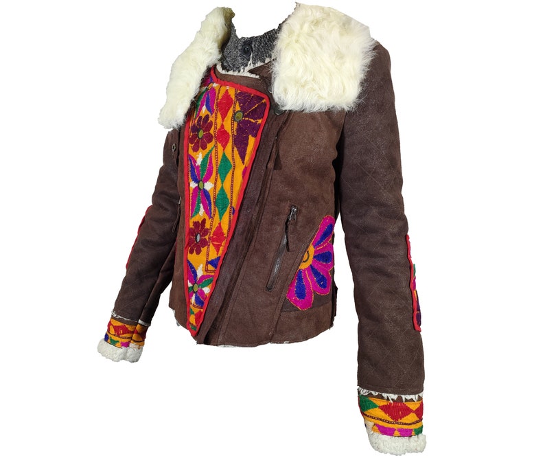 K&ouml;nnte beinhalten: Braune Wildlederjacke mit wei&szlig;em Kunstfellkragen und bunten, gestickten Blumen- und geometrischen Mustern. Die Jacke hat einen diagonalen Rei&szlig;verschluss und dekorative Verzierungen an den &Auml;rmeln.