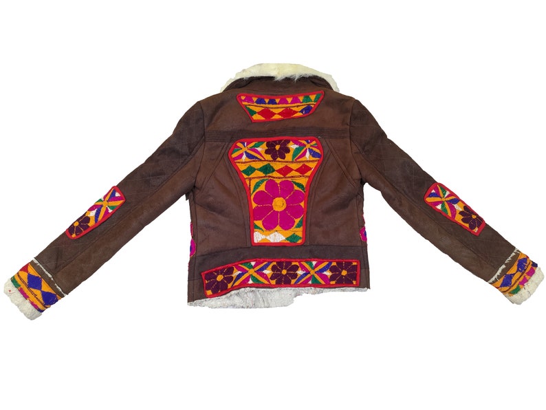 K&ouml;nnte beinhalten: Braune Wildlederjacke mit farbenfrohen, gestickten Blumen- und geometrischen Designs. Die Jacke hat einen cremefarbenen Kunstfellkragen und -futter. Die &Auml;rmel und der R&uuml;cken sind mit leuchtenden Mustern in Rot, Gelb, Blau und Lila verziert.
