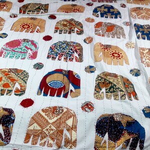 K&ouml;nnte beinhalten: Wei&szlig;e Baumwolldecke mit Patchwork-Design mit bunten Elefanten. Die Elefanten sind aus verschiedenen Stoffen mit verschiedenen Mustern und Farben gefertigt.