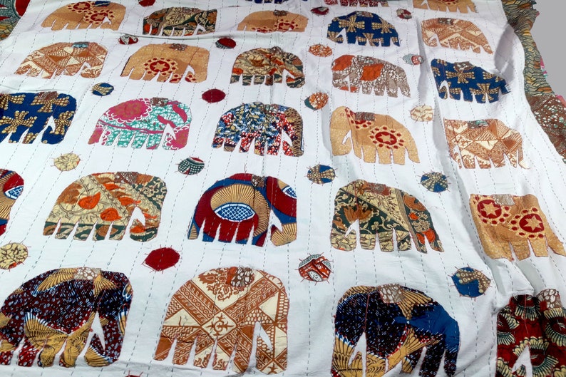 K&ouml;nnte beinhalten: Wei&szlig;e Baumwolldecke mit Patchwork-Design mit bunten Elefanten. Die Elefanten sind aus verschiedenen Stoffen mit verschiedenen Mustern und Farben gefertigt.