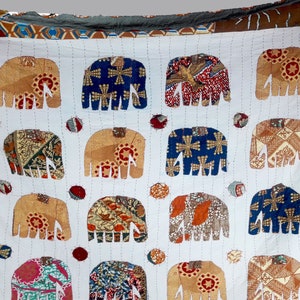 K&ouml;nnte beinhalten: Eine wei&szlig;e Baumwolldecke mit Patchwork-Muster, die mehrere braune, blaue und rote Elefanten zeigt. Die Elefanten sind aus verschiedenen gemusterten Stoffen gefertigt und in einem Gittermuster angeordnet.