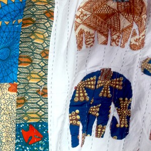 K&ouml;nnte beinhalten: Eine wei&szlig;e Stoffdecke mit bunten Patchwork-Elefantenmotiven. Die Elefanten sind aus verschiedenen Stoffen mit geometrischen Mustern in Blau-, Gr&uuml;n-, Orange- und Braunt&ouml;nen gefertigt.