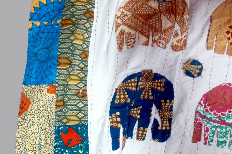 K&ouml;nnte beinhalten: Eine wei&szlig;e Stoffdecke mit bunten Patchwork-Elefantenmotiven. Die Elefanten sind aus verschiedenen Stoffen mit geometrischen Mustern in Blau-, Gr&uuml;n-, Orange- und Braunt&ouml;nen gefertigt.