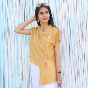 May include: A mustard yellow linen top with a diagonal button closure and short sleeves. The top is asymmetrical and has a relaxed fit.