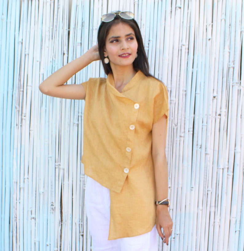 May include: A mustard yellow linen top with a diagonal button closure and short sleeves. The top is asymmetrical and has a relaxed fit.