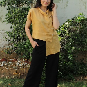 May include: A woman wearing a mustard yellow linen top with a diagonal button closure and black wide-leg pants.