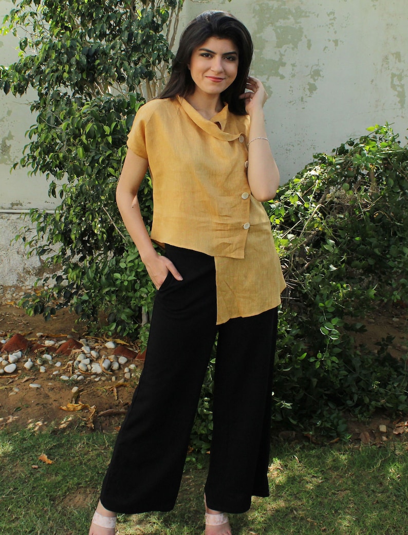 May include: A woman wearing a mustard yellow linen top with a diagonal button closure and black wide-leg pants.