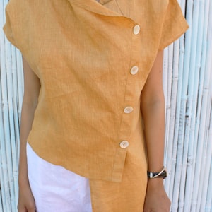 May include: A mustard yellow linen shirt with a asymmetrical hemline and a row of buttons down the side.