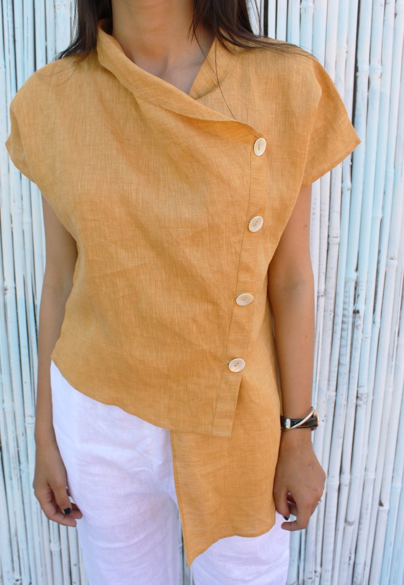 May include: A mustard yellow linen shirt with a asymmetrical hemline and a row of buttons down the side.