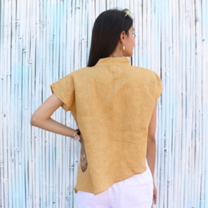 May include: A mustard yellow linen shirt with a high neckline and short sleeves. The shirt has a slightly asymmetrical hemline.