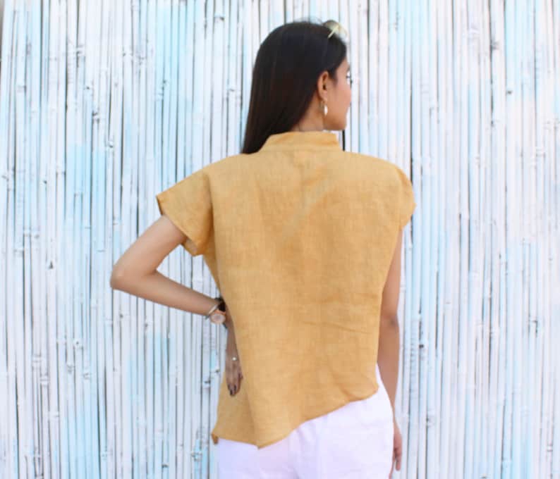 May include: A mustard yellow linen shirt with a high neckline and short sleeves. The shirt has a slightly asymmetrical hemline.