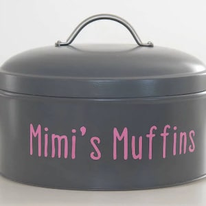 May include: A grey metal cookie tin with a silver handle and the words "Mimi's Muffins" written in pink letters.