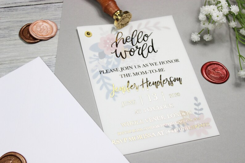 Op de afbeelding: Een witte babyshower-uitnodiging met gouden letters. De uitnodiging luidt "hello world" en bevat de tekst "Please join us as we honor the mom-to-be Jennifer Henderson, June 13, 2020, at 3 o'clock, Whole Venue, London. RSVP Morissa at +44 07812..."