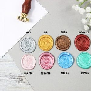 Op de afbeelding: Assortiment van waszegels in verschillende kleuren, waaronder zilver, goud, brons, antiek rood, lichtroze, blush roze, lichtblauw en turquoise. Elke zegel heeft een ontwerp met twee voetafdrukken.