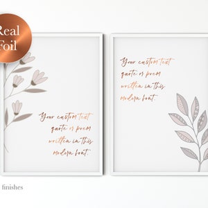 Op de afbeelding: Twee afdrukbare wandkunstprints met witte frames. Elke print heeft een eenvoudig bloemenontwerp in grijstinten en roze. De tekst "Your custom text quote or poem written in this modern font." is in koperfolie op elke print gedrukt.