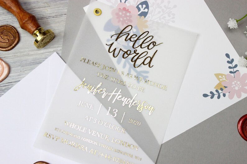 Op de afbeelding: Een witte en grijze uitnodiging met gouden folielettering die "hello world" en "Wordt u alstublieft bij ons om de aanstaande moeder Jennifer Henderson te eren op 13 juni 2020 om 15:00 uur op de hele locatie, locatie" zegt.