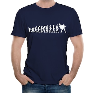 May include: A navy blue t-shirt with a white graphic showing the evolution of man, ending with a superhero. The design progresses from ape to a caped figure. The shirt has a classic crew neck.