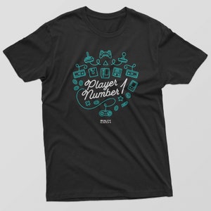 Op de afbeelding: Zwart T-shirt met een turquoiseblauw ontwerp van retro-videogamescontrollers en de tekst "Player Number 1".
