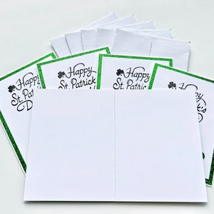 May include: A stack of blank greeting cards with a green glitter border and the text "Happy St. Patrick's Day" printed on the front.