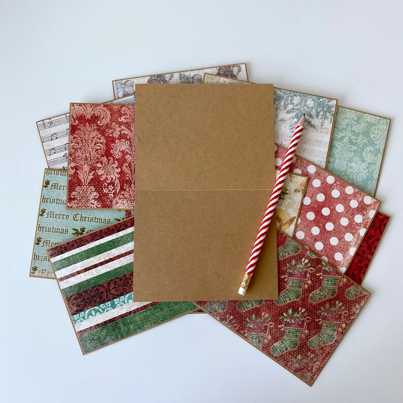 May include: A stack of patterned paper with a brown card and a red and white striped pencil on top. The paper has a variety of Christmas-themed patterns, including red and white polka dots, green and white stripes, and a red and white floral pattern. The card is blank and can be used for crafting or scrapbooking.