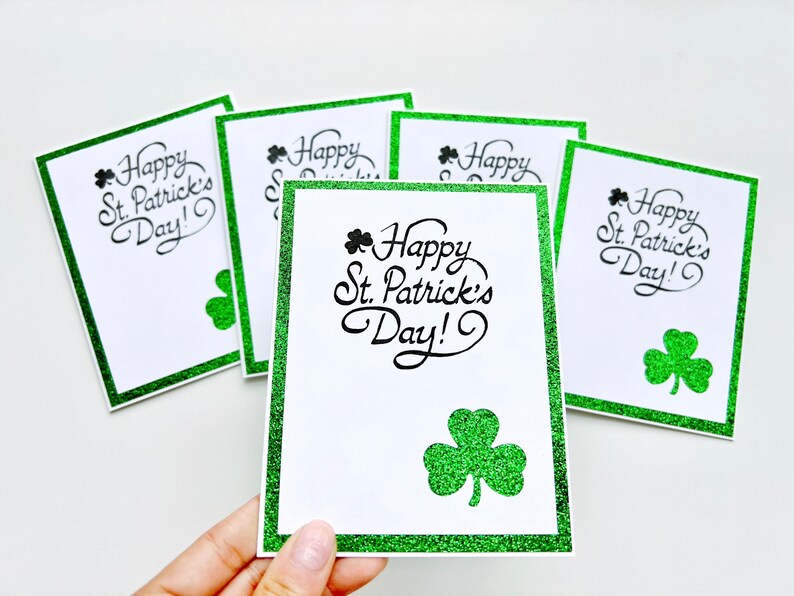 May include: Five green glitter-edged cards with the text "Happy St. Patrick's Day!" in black cursive lettering and a green shamrock graphic.