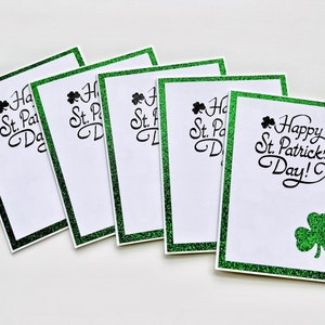 May include: Five green glitter cards with a shamrock design and the text "Happy St. Patrick's Day!" printed in black.