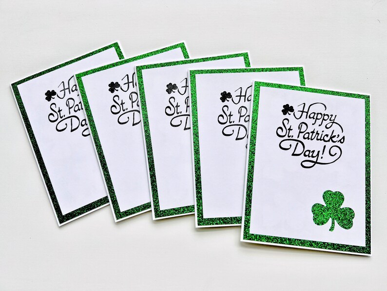 May include: Five green glitter cards with a shamrock design and the text "Happy St. Patrick's Day!" printed in black.