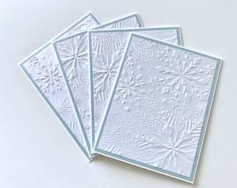 May include: Four white greeting cards with a raised snowflake design and a light blue border.
