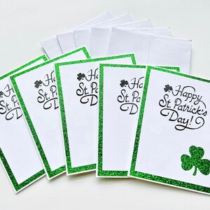 May include: Six blank greeting cards with a green glitter border and the text "Happy St. Patrick's Day!" on one card. The cards are white with a shamrock design on the card with the text.