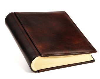 May include: A brown leather-bound photo album with a flap closure. The album has a curved spine and a rectangular shape. The pages are cream-colored, and the cover has a rich, textured appearance.