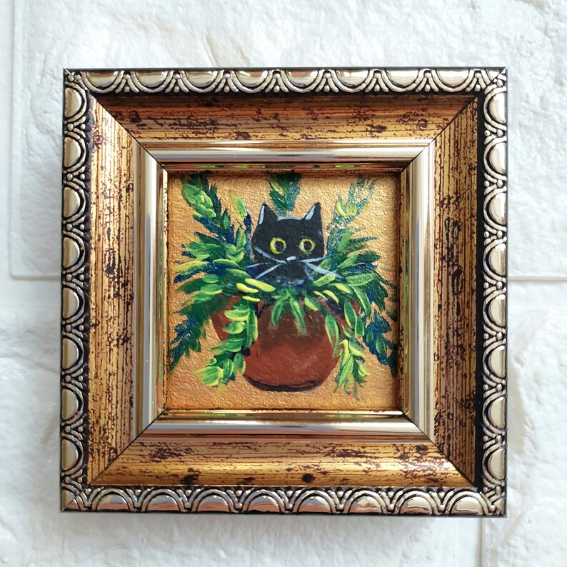 May include: A black cat peeking out from a pot of green plants, painted in a whimsical style. The painting is framed in a gold and silver ornate frame.