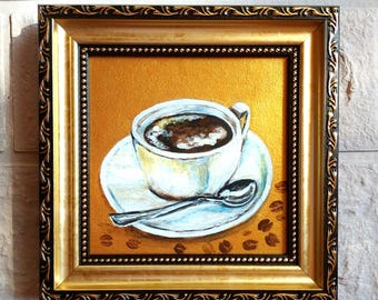 May include: A framed painting of a white coffee cup and saucer on a gold background. The cup is filled with dark coffee and a silver spoon rests on the saucer. Scattered coffee beans are painted on the surface. The frame is ornate gold and black.