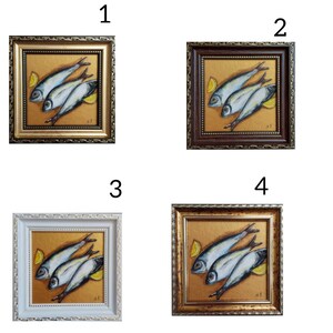May include: Four square framed paintings featuring a still life of three silver fish and two yellow lemon wedges on a textured gold background. Each frame has a distinct finish: metallic gold, dark brown, white, and an antique gold tone.