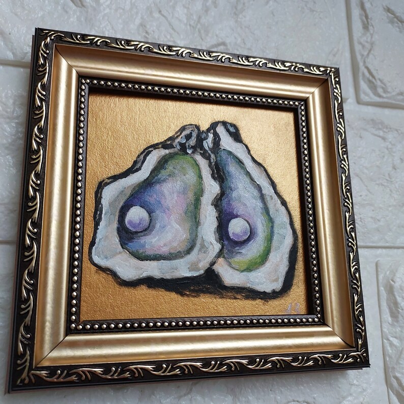 May include: A square painting in a decorative gold and dark brown frame featuring two open oyster shells with iridescent green, purple, and white interiors, each containing a single white pearl, set against a solid metallic gold background.