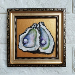 May include: A square painting of two open oyster shells with iridescent purple and green interiors, each containing a white pearl. The artwork is set against a metallic gold background and enclosed in a decorative dark brown and gold frame.