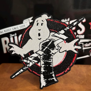 May include: Embroidered patch featuring the Ghostbusters logo. The design includes a white ghost figure, a black and red circle, and a proton pack. The patch has a black border and the text "RUGGED BUDDY SINCE 2009" is visible in the background.